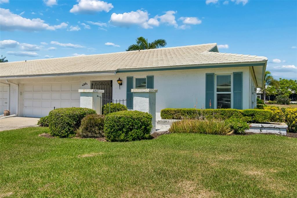 A single-story white house with a garage, blue shutters, and a manicured lawn — 7310 9TH AVE W UNIT 5834, BRADENTON, FL