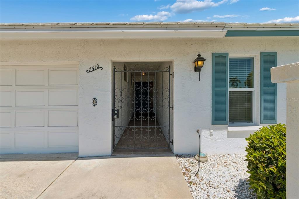 The exterior of a white house features a garage, a gated entryway, and blue shutters — 7310 9TH AVE W UNIT 5834, BRADENTON, FL