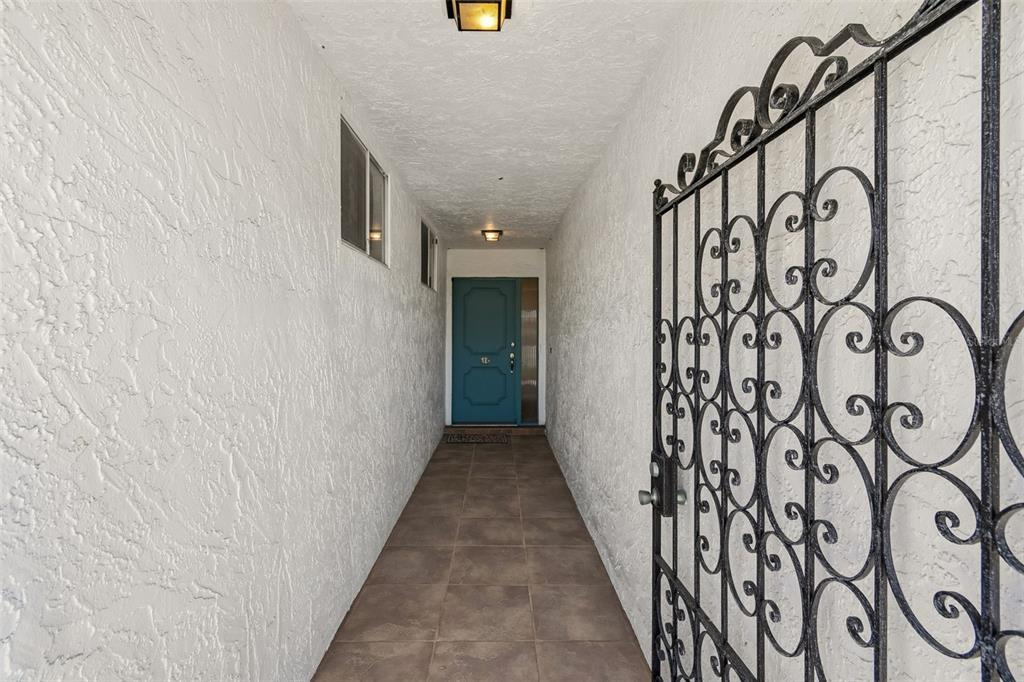 A narrow outdoor entryway features white stucco walls, tile flooring, and a decorative iron gate — 7310 9TH AVE W UNIT 5834, BRADENTON, FL