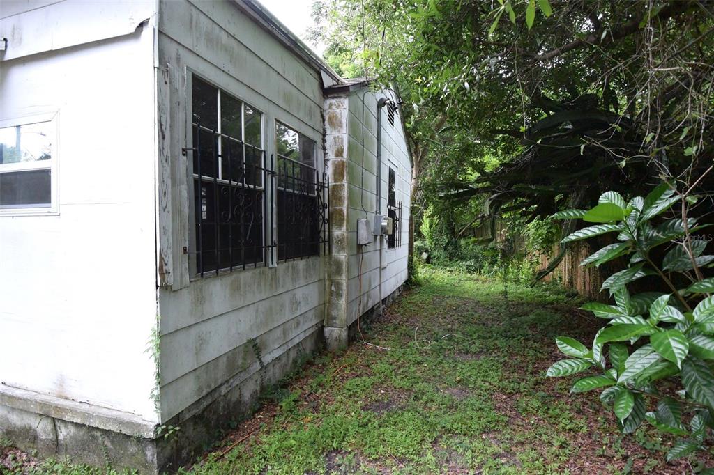 The exterior side of a white house features windows with black security bars and overgrown landscaping — 1422 W HUMPHREY STREET, TAMPA, FL