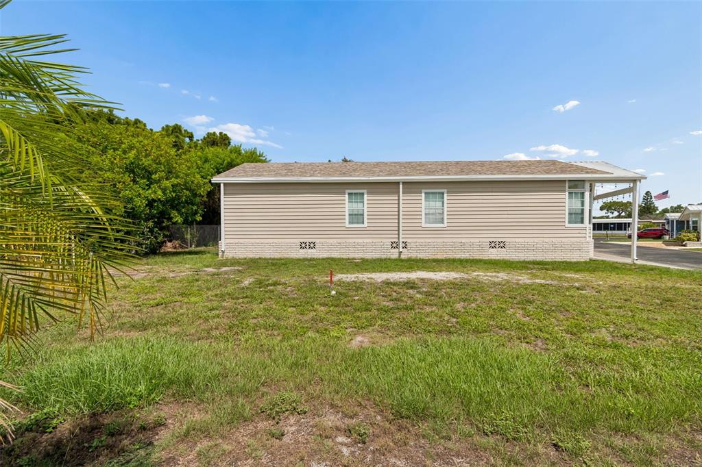 A grassy vacant lot sits between two manufactured homes under a clear blue sky — 9790 66TH STREET N UNIT 365, PINELLAS PARK, FL