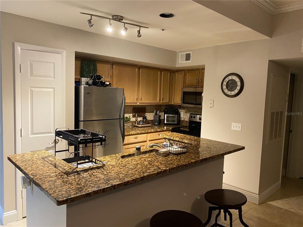 A kitchen features a granite-topped breakfast bar, stainless steel refrigerator, and wooden cabinetry — 482 N PIN OAK PLACE UNIT 304, LONGWOOD, FL