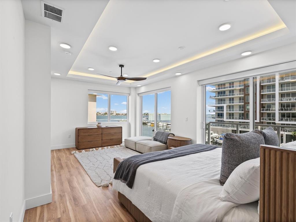 A modern bedroom features a tray ceiling, wood flooring, and a balcony overlooking a marina — 868 N OSCEOLA AVENUE, CLEARWATER, FL