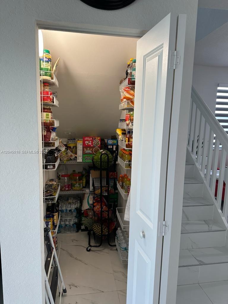 A walk-in pantry with white wire shelving, tile flooring, and food storage under a staircase — 12760 SW 215th Ter, Miami FL 33177, MIAMI, FL