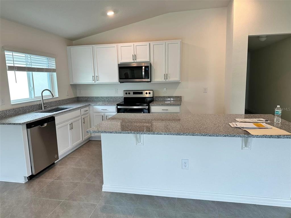 A kitchen features white cabinets, granite countertops, stainless steel appliances, and a central island — 3863 AXIS VALLEY PLACE, ST CLOUD, FL