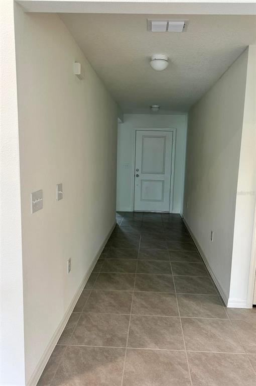 A hallway with light-colored walls and tiled flooring leads to a white front door — 3863 AXIS VALLEY PLACE, ST CLOUD, FL