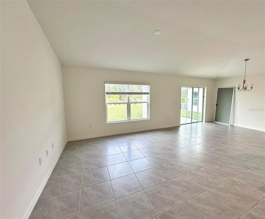 An empty living room with light-colored tile flooring, white walls, and a sliding glass door — 3863 AXIS VALLEY PLACE, ST CLOUD, FL