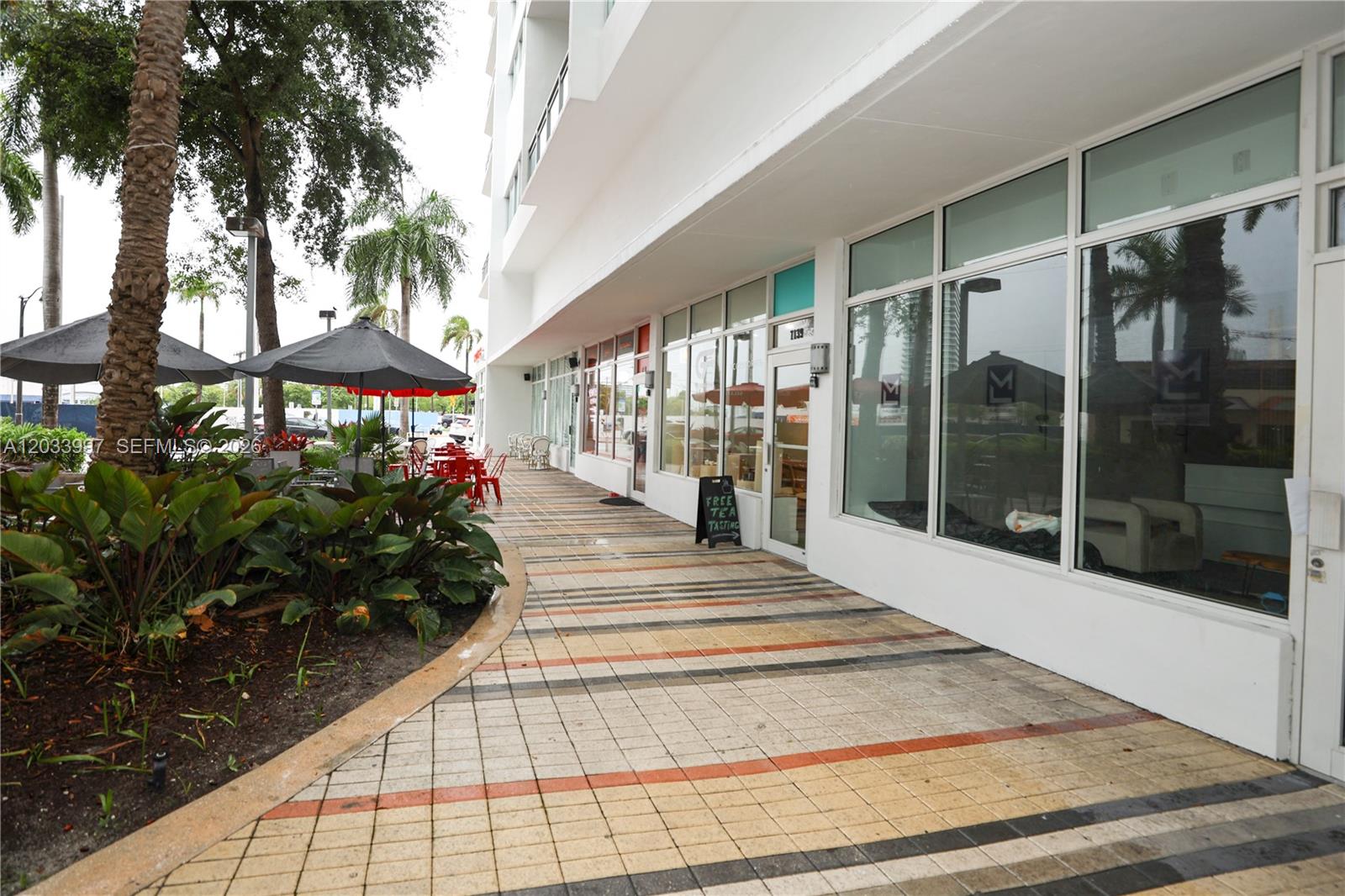 A sidewalk runs along the exterior of a modern building with large glass storefront windows — 7135 Collins Ave # 735, Miami Beach FL 33141, MIAMI BEACH, FL