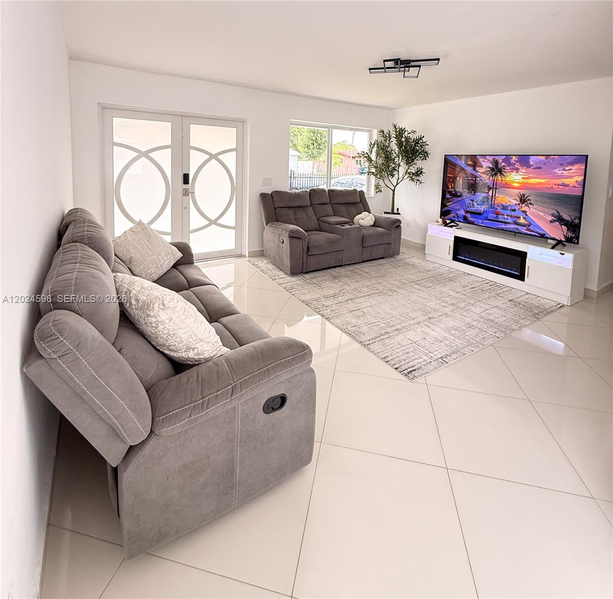 A living room features gray reclining sofas, a television, and a fireplace on tile floors — 20130 SW 106th Ave, Cutler Bay FL 33189, CUTLER BAY, FL