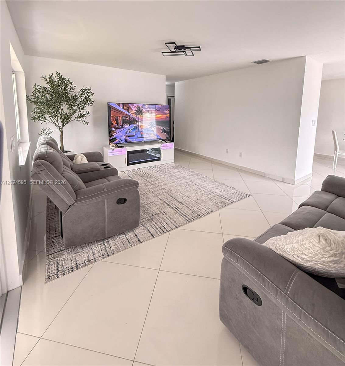 A living room features gray reclining sofas, a television on a media console, and tile flooring — 20130 SW 106th Ave, Cutler Bay FL 33189, CUTLER BAY, FL