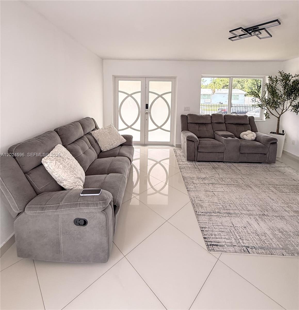 A living room features gray reclining sofas, a patterned area rug, and white tile floors — 20130 SW 106th Ave, Cutler Bay FL 33189, CUTLER BAY, FL