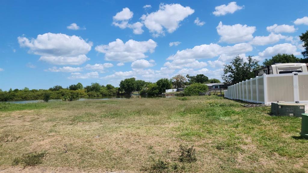 A vacant, grassy lot sits next to a white vinyl fence near a body of water — 3143 JACKSON DRIVE, HOLIDAY, FL