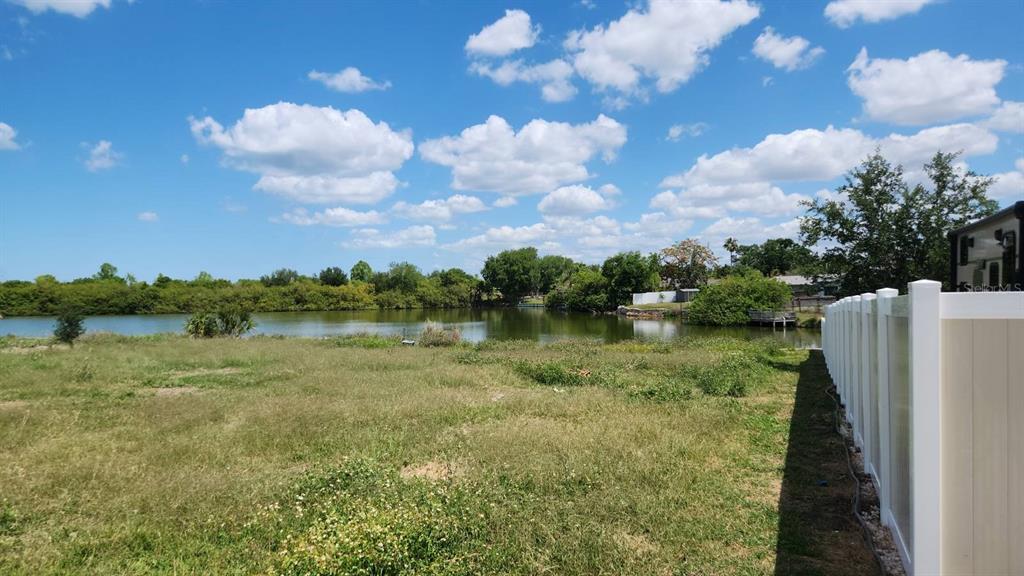 A grassy backyard overlooks a pond with a white vinyl fence on the right side — 3143 JACKSON DRIVE, HOLIDAY, FL