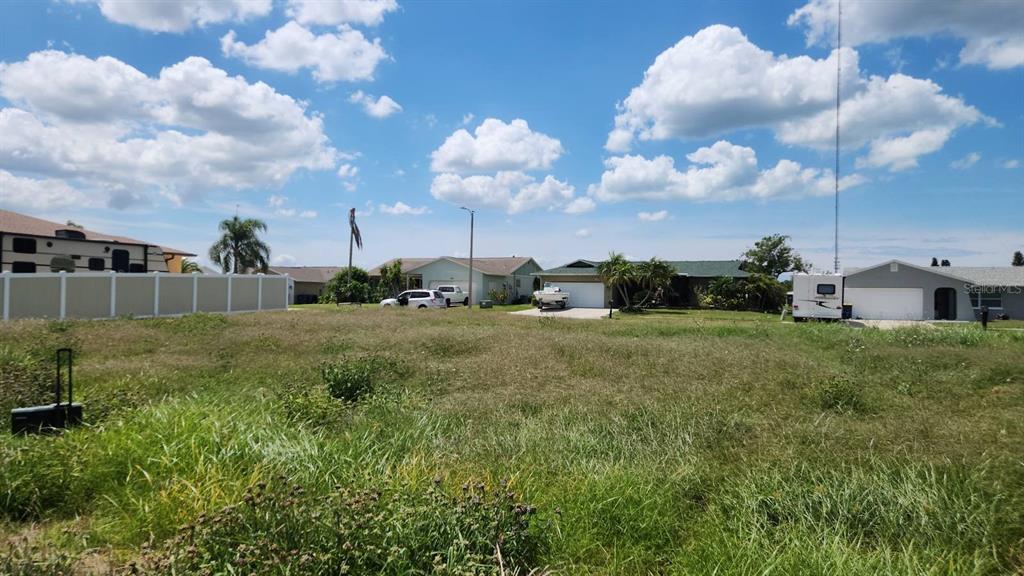 A vacant, grassy residential lot sits in front of several single-story houses under a cloudy sky — 3143 JACKSON DRIVE, HOLIDAY, FL