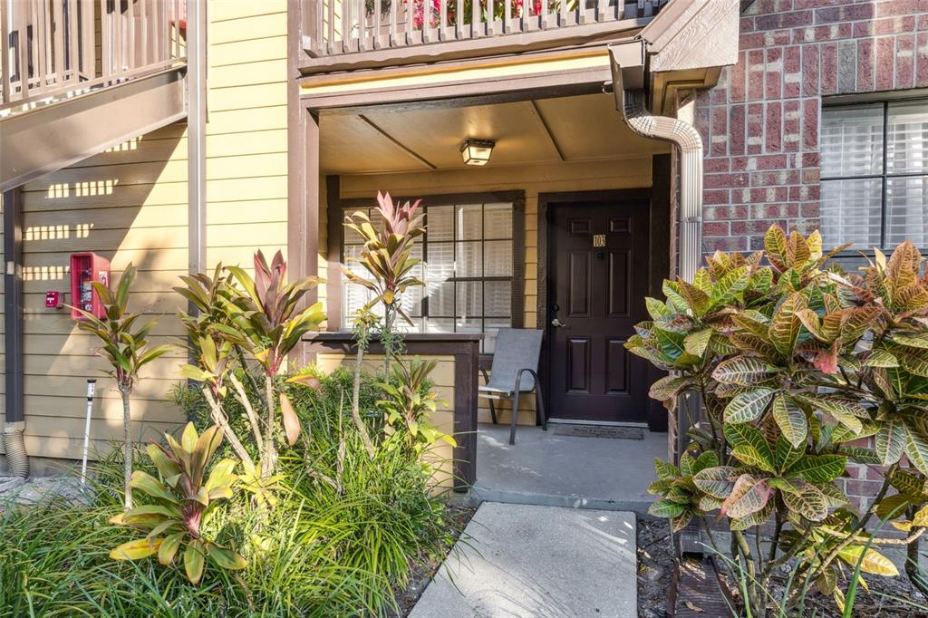 The exterior entrance of a ground-floor apartment features a dark door, a small patio, and landscaping — 415 LAKEPOINTE DRIVE UNIT 103, ALTAMONTE SPRINGS, FL