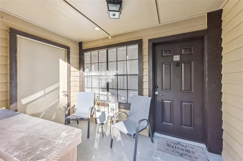 A covered patio features two gray chairs, a small table, and a dark brown front door — 415 LAKEPOINTE DRIVE UNIT 103, ALTAMONTE SPRINGS, FL