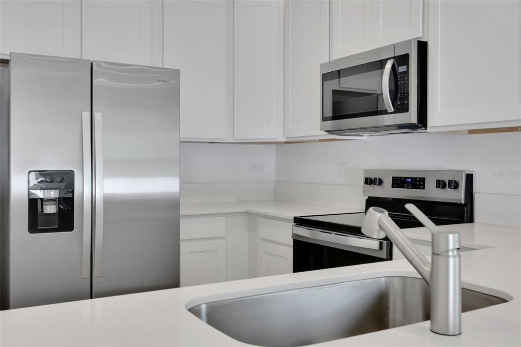 A modern kitchen features white cabinets, stainless steel appliances, and white quartz countertops — 733 SAILOR GROVE LANE, JACKSONVILLE, FL