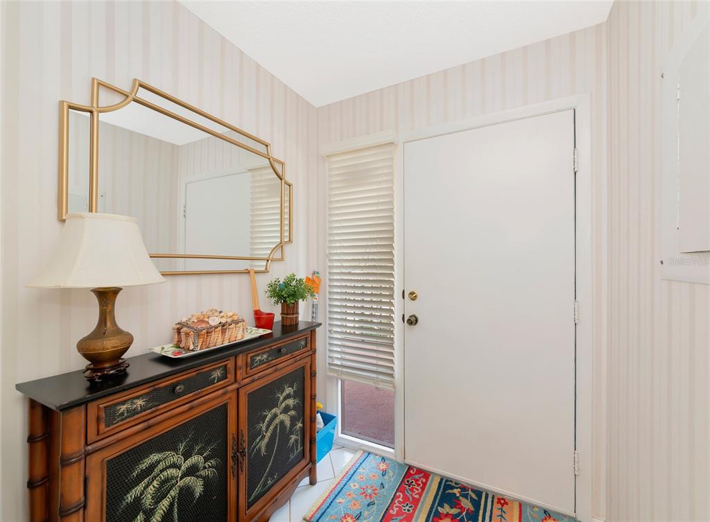 An entryway features a console table, a gold-framed mirror, and a white door with blinds — 6423 EGRET LANE UNIT 406, BRADENTON, FL