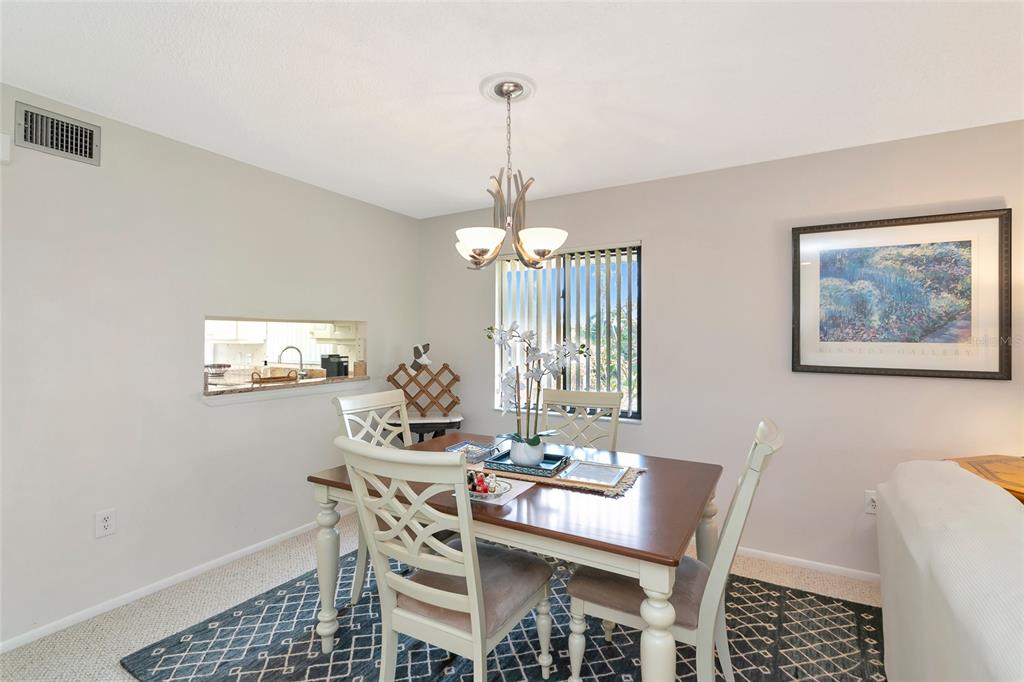 A dining room features a wooden table, four chairs, a chandelier, and a pass-through window — 6423 EGRET LANE UNIT 406, BRADENTON, FL