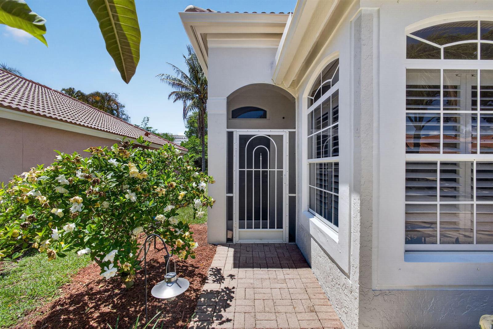 A white house exterior features a paved walkway, a screen door, and a flowering bush — 5137 Elpine Way, Riviera Beach FL 33418, RIVIERA BEACH, FL