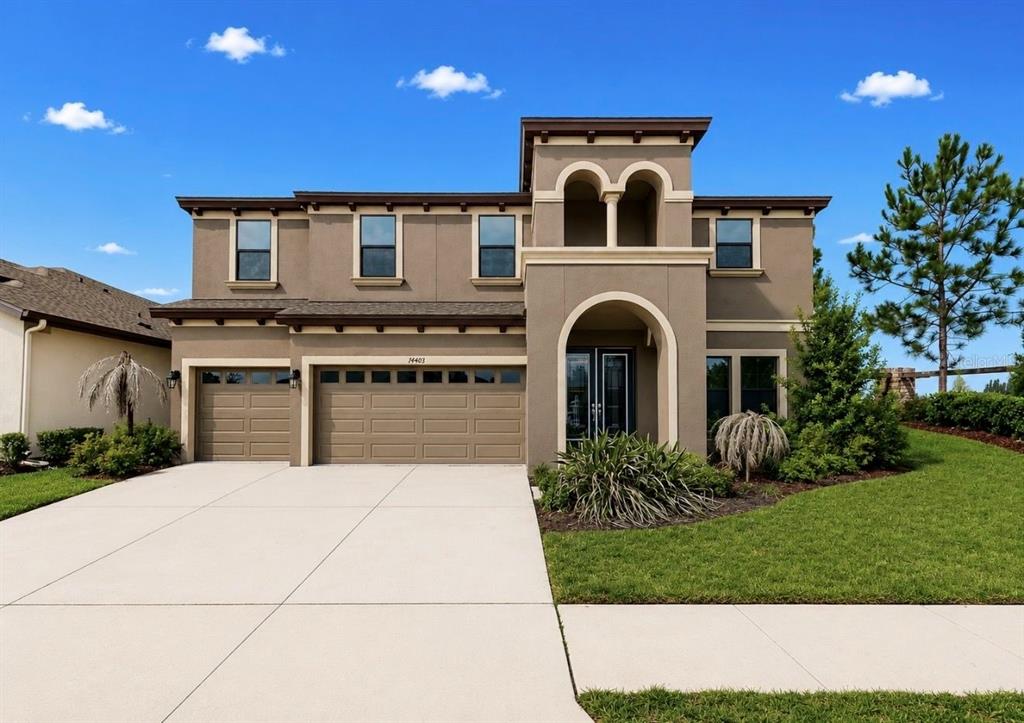 A two-story suburban house with a tan stucco exterior, a three-car garage, and a driveway — 14403 WOODLAND SPUR DRIVE, LITHIA, FL