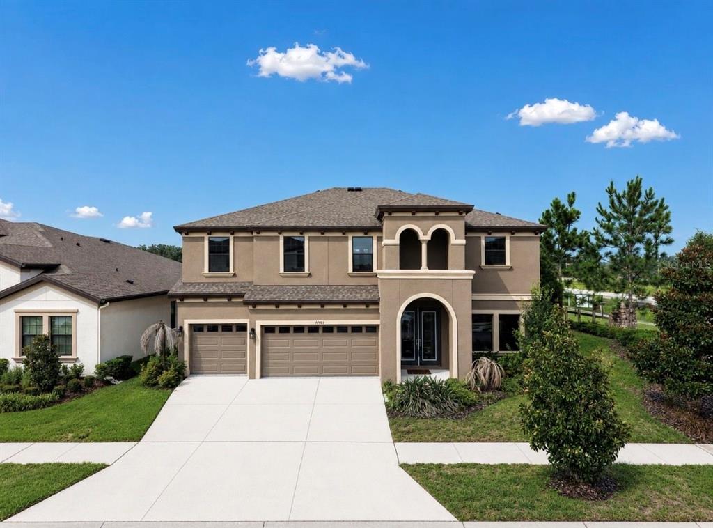 A two-story tan stucco house with a three-car garage and a covered arched entryway — 14403 WOODLAND SPUR DRIVE, LITHIA, FL