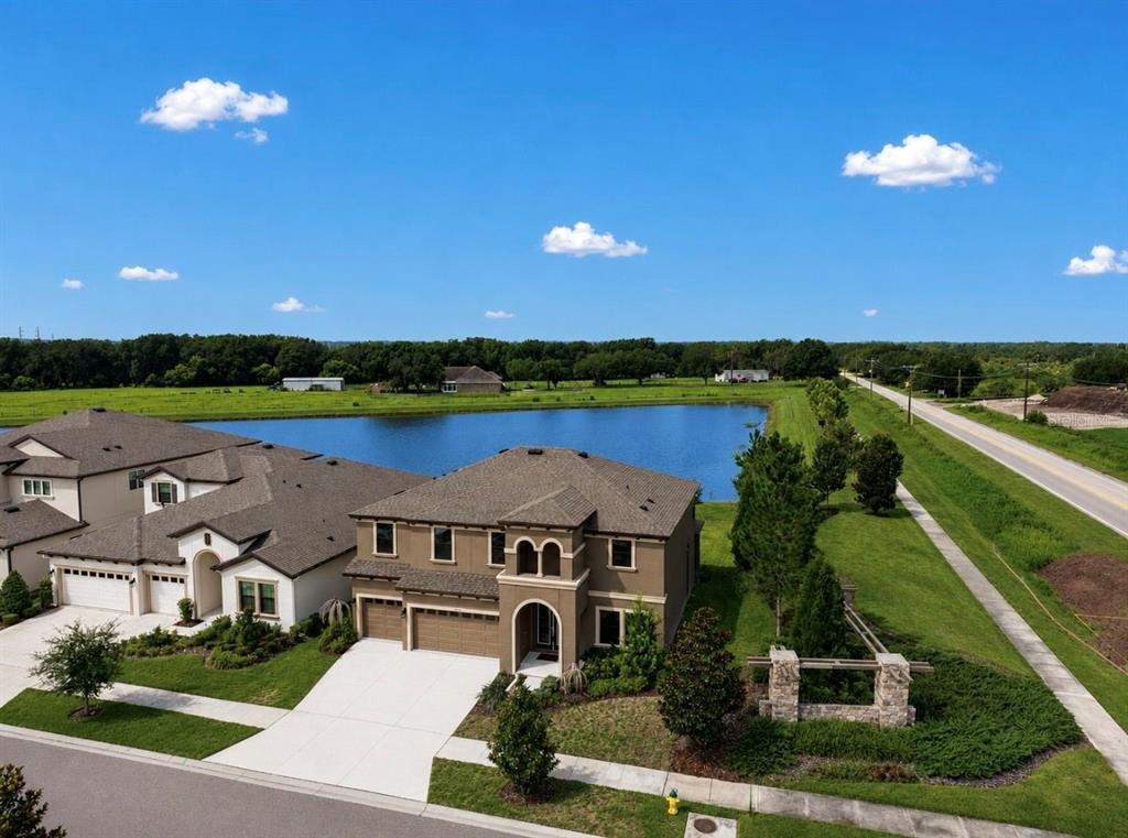 An aerial view shows a two-story suburban house with a lake in the background — 14403 WOODLAND SPUR DRIVE, LITHIA, FL