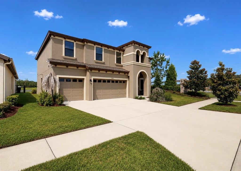A two-story tan stucco house with a three-car garage and a concrete driveway — 14403 WOODLAND SPUR DRIVE, LITHIA, FL