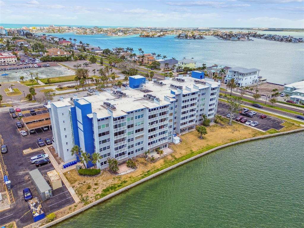An aerial view shows a multi-story apartment building situated along a waterfront with parking lots — 500 TREASURE ISLAND CAUSEWAY UNIT 607, ST PETERSBURG, FL
