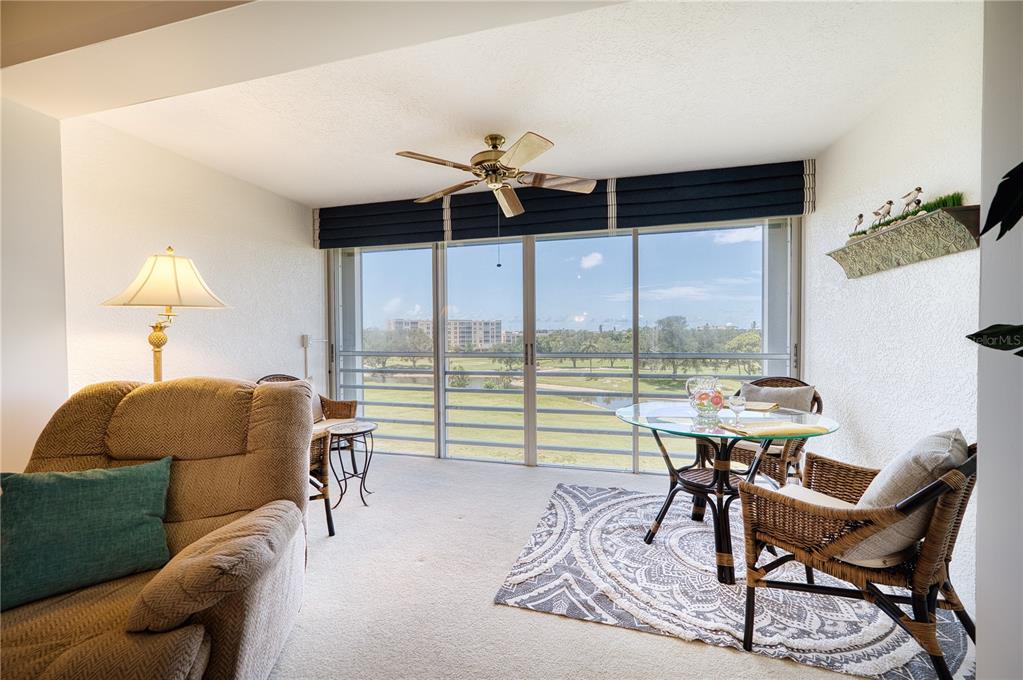 A sunroom features a glass dining table, wicker chairs, carpeted floors, and a golf course view — 3780 PINEBROOK CIRCLE UNIT 504, BRADENTON, FL