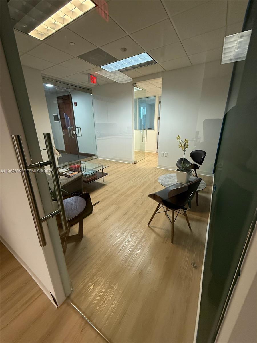 A modern office waiting area features light wood flooring, glass doors, and contemporary seating — 1101 Brickell Ave, FL 33131, FL