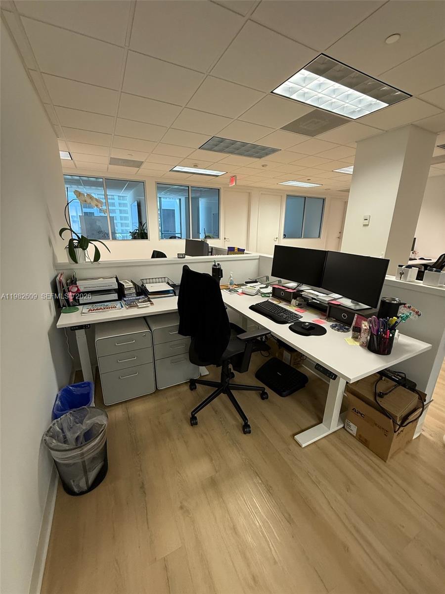 A modern office cubicle features a white L-shaped desk, dual monitors, and light wood flooring — 1101 Brickell Ave, FL 33131, FL