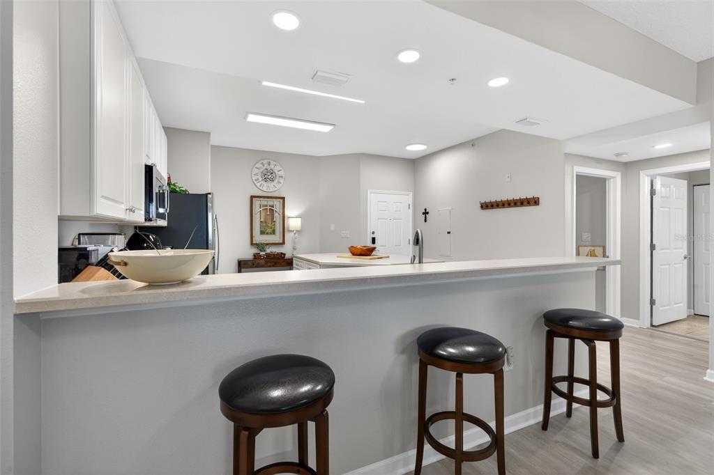 A kitchen features a breakfast bar with three stools, white cabinets, and light-colored flooring — 80 SURFVIEW DRIVE UNIT 811, PALM COAST, FL