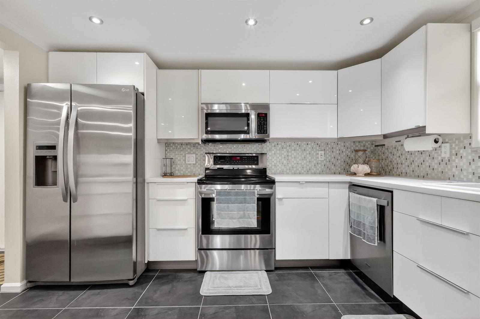 A modern kitchen features white cabinets, stainless steel appliances, a mosaic backsplash, and dark tile flooring — 720 N Dixie Highway # 604, Lantana FL 33462, LANTANA, FL