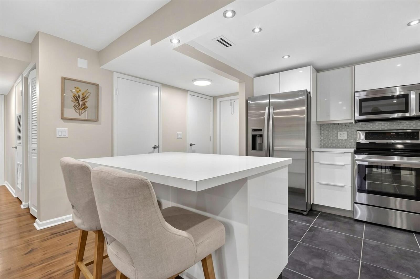 A modern kitchen features a white island, stainless steel appliances, and dark tile flooring — 720 N Dixie Highway # 604, Lantana FL 33462, LANTANA, FL