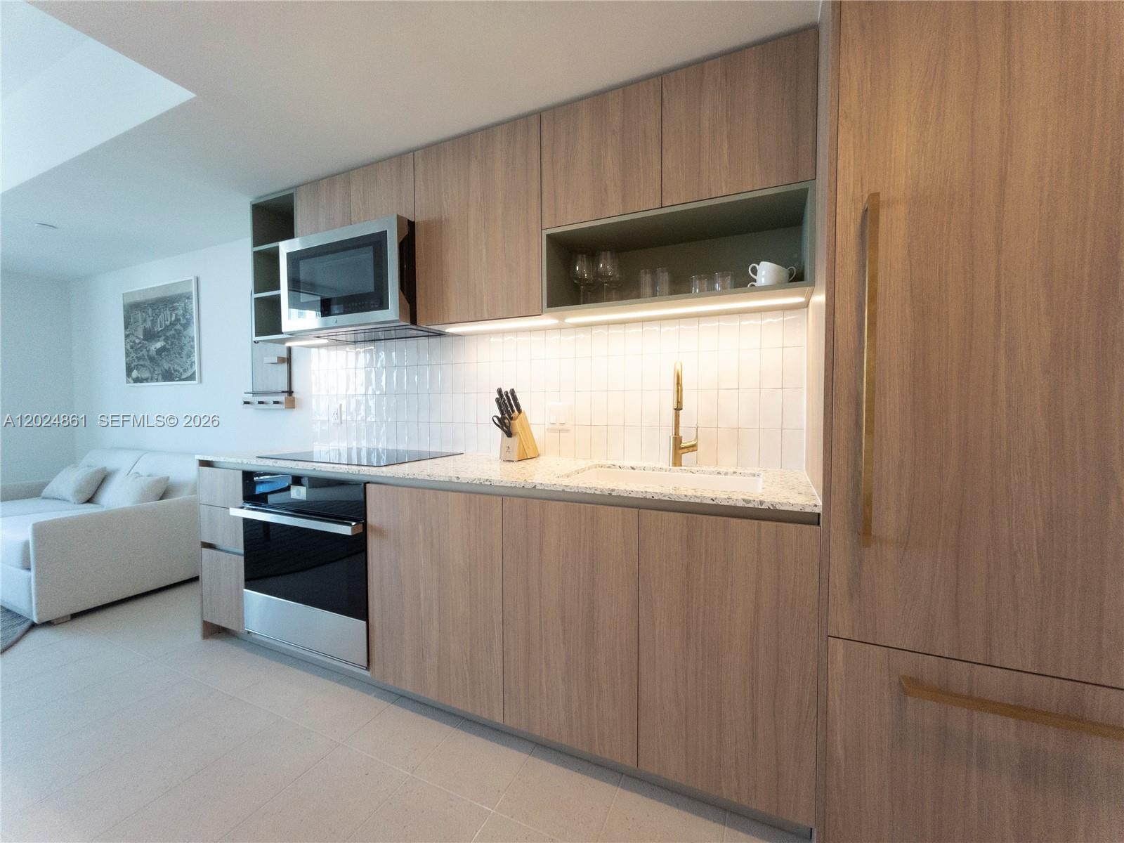 A modern kitchen features wood-grain cabinets, white tile backsplash, and stainless steel appliances — 159 NE 6th St # 2508, Miami FL 33132, MIAMI, FL