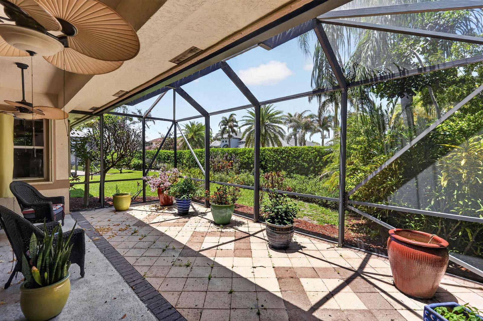 A screened-in patio with tiled flooring, potted plants, and outdoor furniture overlooking a landscaped yard — 7982 SE Hempstead Circle, Hobe Sound FL 33455, HOBE SOUND, FL