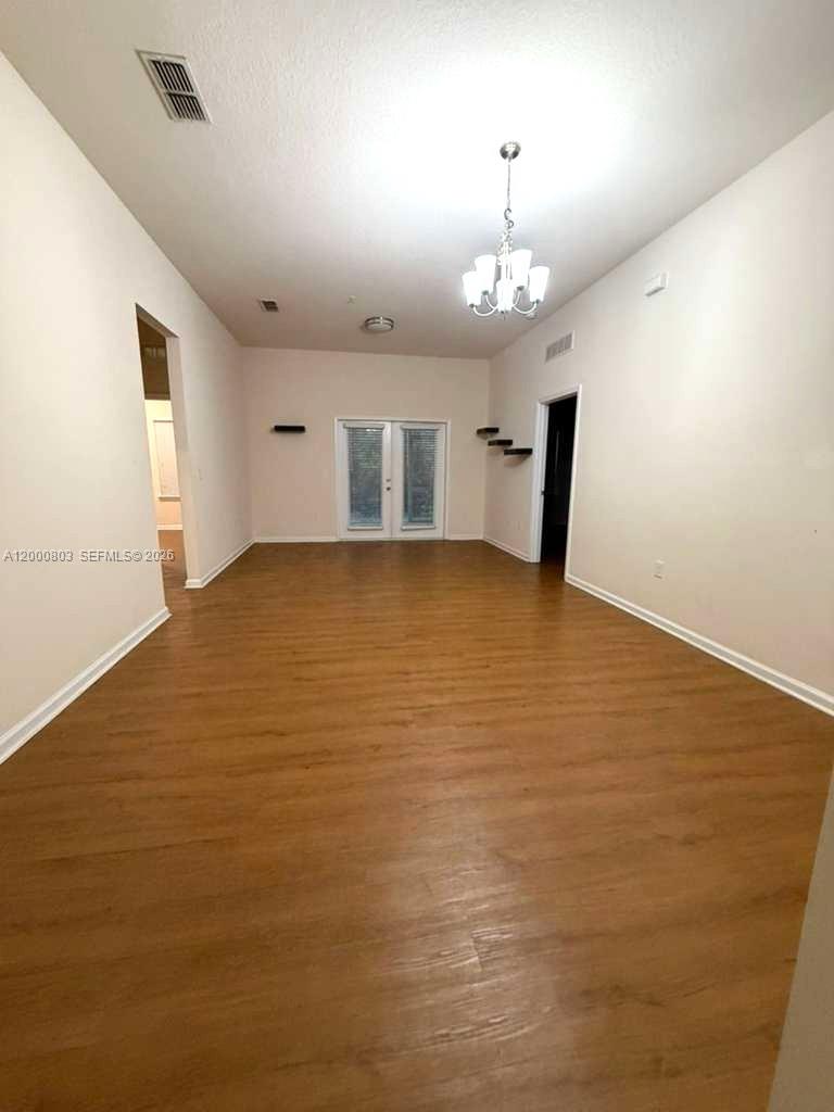 An empty room features light wood-look flooring, white walls, a chandelier, and glass double doors — 2105 Golden Lake Loop St, St Augustine FL 32084, ST AUGUSTINE, FL