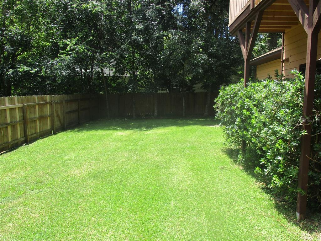 A grassy backyard features a wooden privacy fence and a house with a deck — 1631 NW 94TH STREET, GAINESVILLE, FL