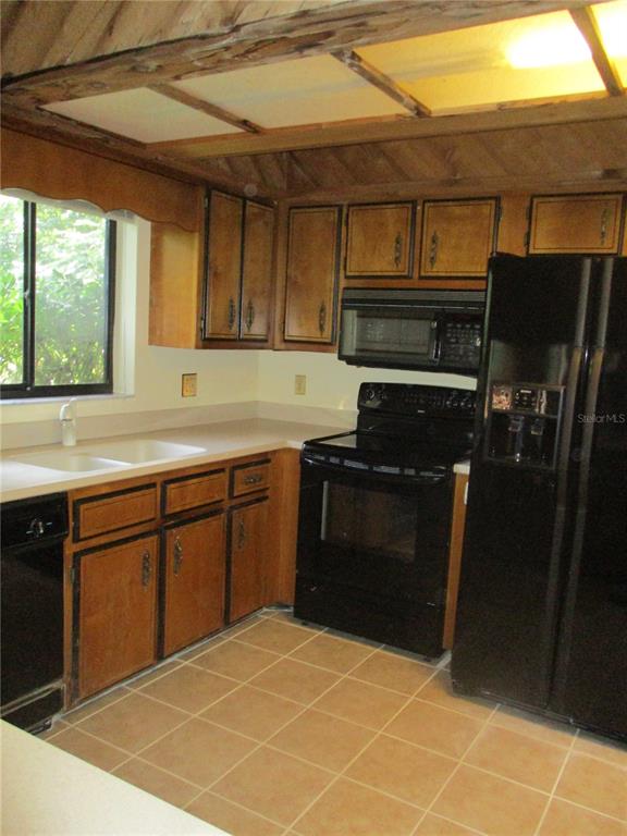 A kitchen features wood cabinets, black appliances, a double sink, and a tiled floor — 1631 NW 94TH STREET, GAINESVILLE, FL