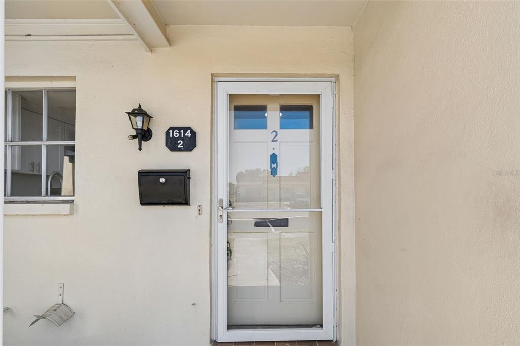 A white front door with a storm door, a black mailbox, and a house number sign — 1614 S LAKE AVENUE UNIT 2, CLEARWATER, FL