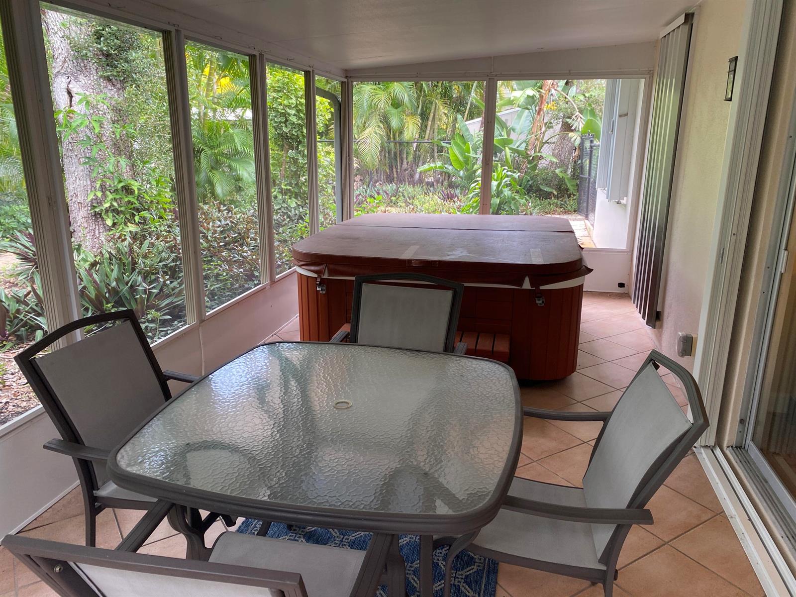 A screened-in patio features a glass-top dining set, tile flooring, and a covered hot tub — 535 Flamevine Lane, Vero Beach FL 32963, VERO BEACH, FL