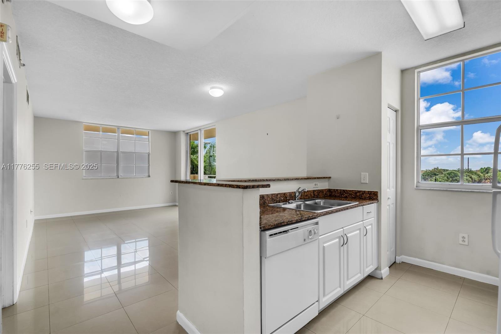 A kitchen with white cabinets and granite countertops overlooks an open-plan living area with tile — 215 SW 42nd Ave # 402, Miami FL 33134, MIAMI, FL