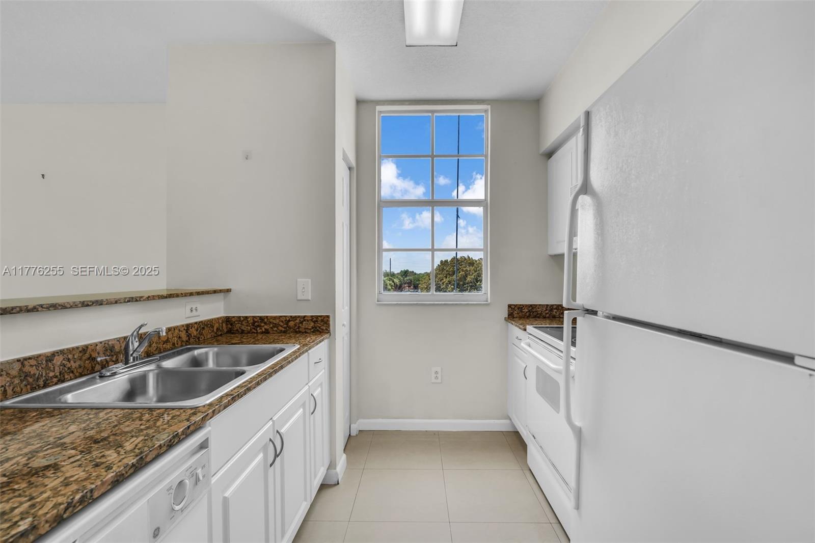 A galley kitchen features white cabinets, granite countertops, a double sink, and a window view — 215 SW 42nd Ave # 402, Miami FL 33134, MIAMI, FL