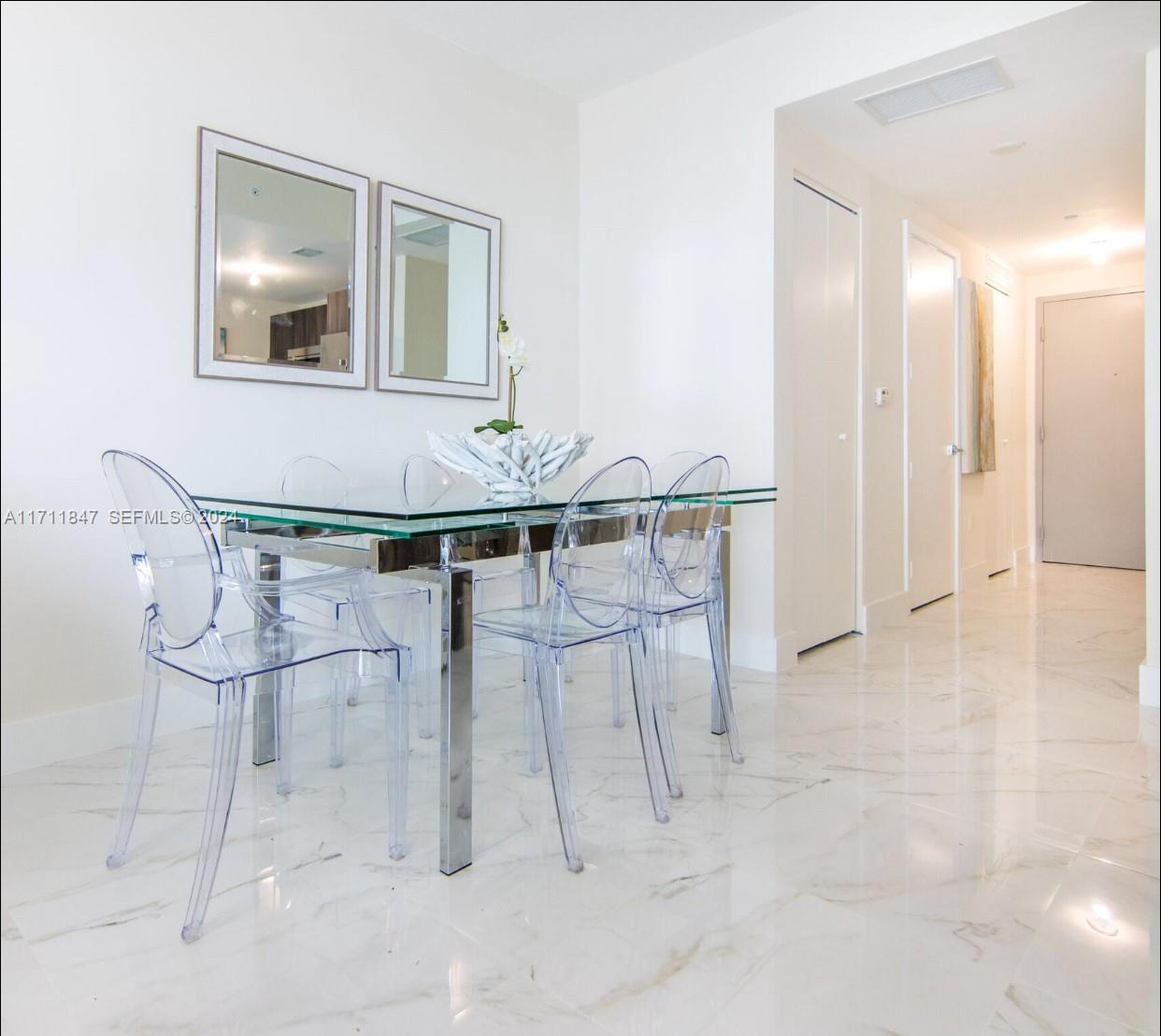 A dining area features a glass-topped table, clear acrylic chairs, and white marble flooring — 488 NE 18th St # 2705, Miami FL 33132, MIAMI, FL