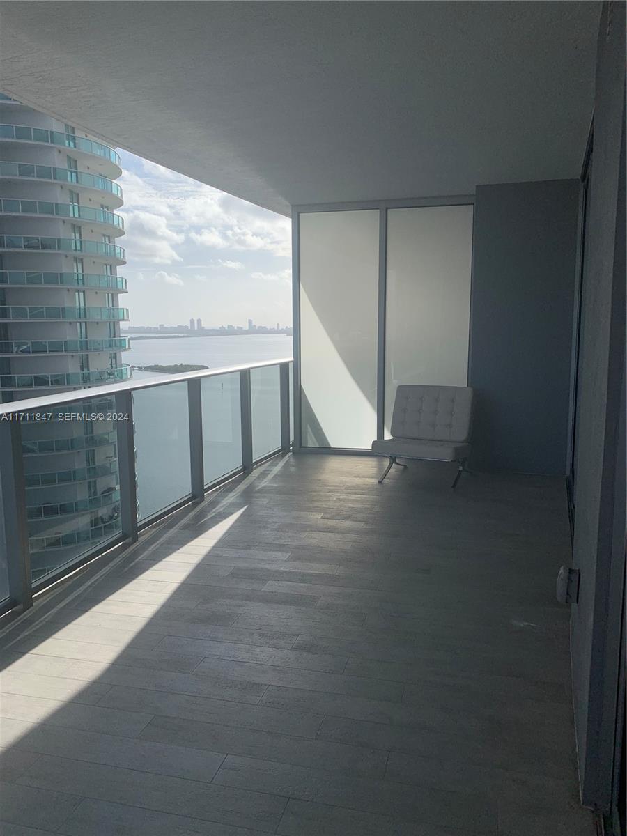 A balcony with wood-look tile flooring, a glass railing, and a single chair overlooking water — 488 NE 18th St # 2705, Miami FL 33132, MIAMI, FL