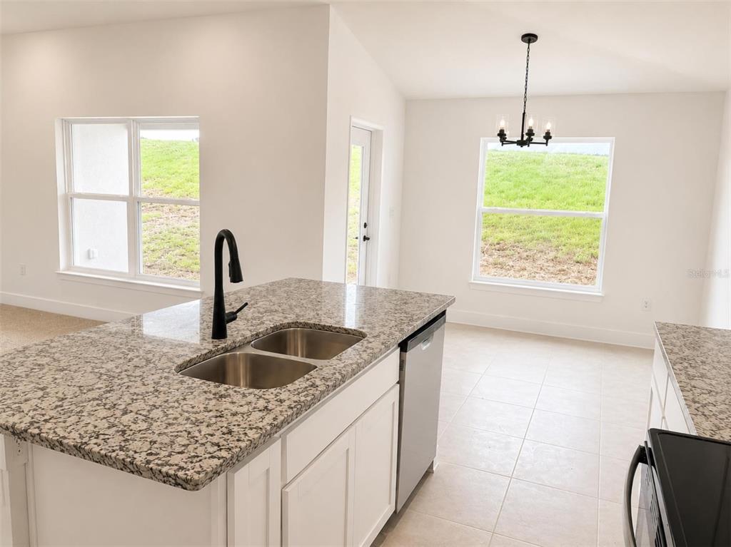 A carpeted room with white walls and a window sits adjacent to a granite-topped kitchen — 1635 ANN ROSE WAY, LEESBURG, FL