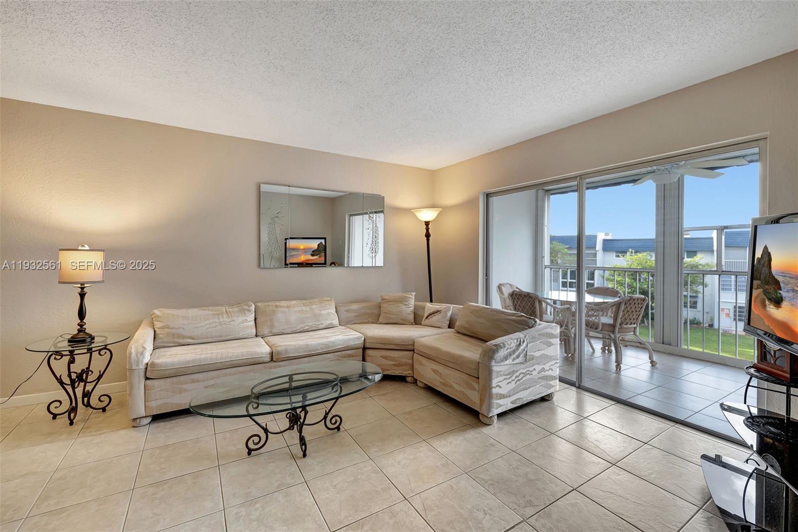 A living room features a sectional sofa, glass coffee table, and sliding doors to a balcony — 7897 Golf Circle Dr # 309, Margate FL 33063, MARGATE, FL