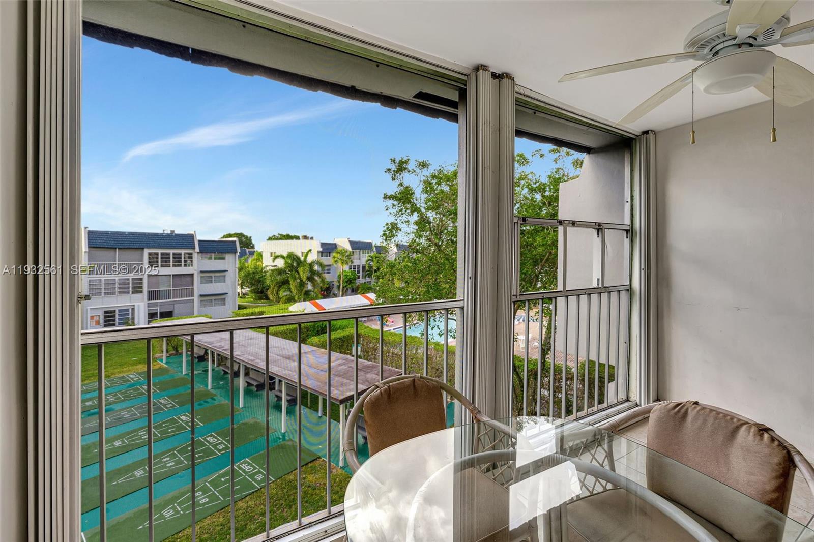 A screened-in balcony overlooks a shuffleboard court and a swimming pool area — 7897 Golf Circle Dr # 309, Margate FL 33063, MARGATE, FL