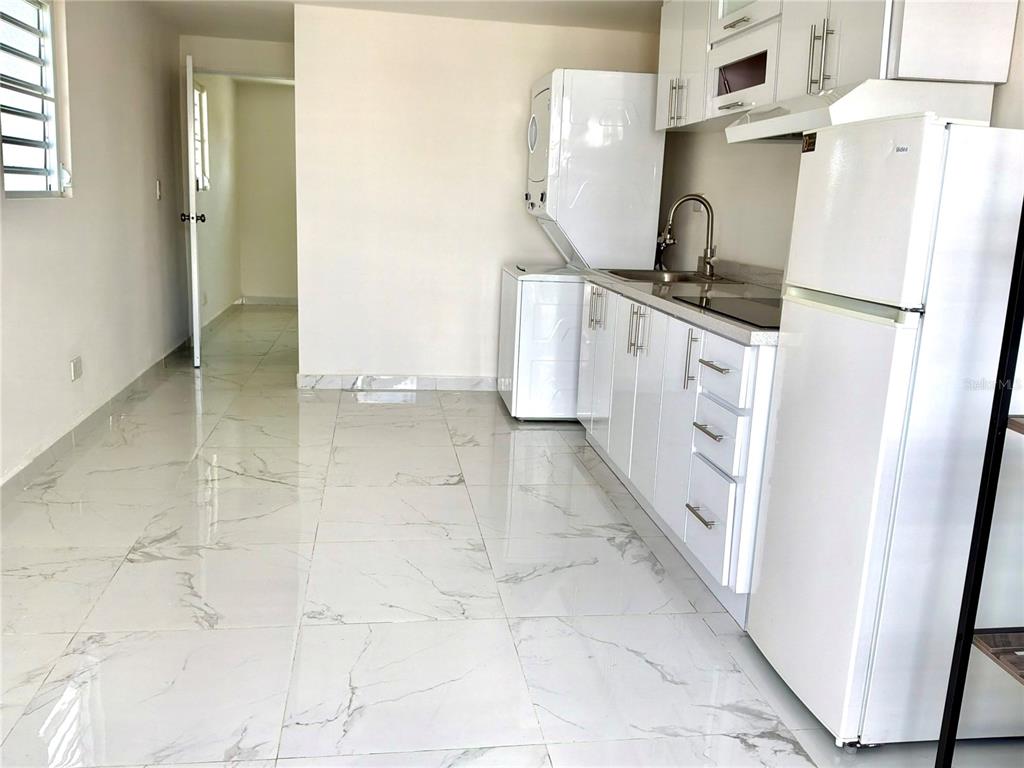 A kitchen features white cabinets, a refrigerator, a stacked washer-dryer, and light marble-patterned tile flooring — 312 Loiza LAS CUMBRES #II, SAN JUAN, PR